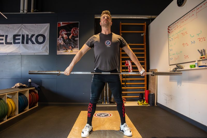 Een lifter trekt de stang hoog op in een clean pull, met de platen op de vloer van de zaal.
